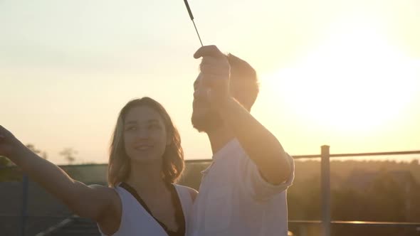 Couple people on roof at sunset on summer evening during party holding sparklers alt
