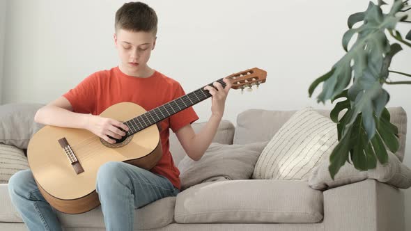 A Teenage Boy Plays the Guitar While Sitting on a Sofa in a Bright Room alt