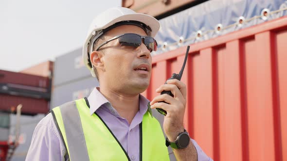 Engineer foreman talking on walkie-talkie with colleague in container warehouse alt