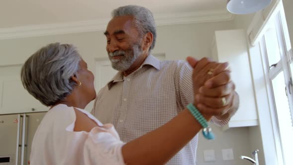 Side view of senior black couple dancing together in kitchen at comfortable home 4k alt