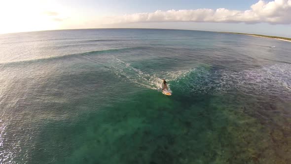 Aerial shot of young woman sup standup paddleboard surfing on a wave in the Caribbean. alt