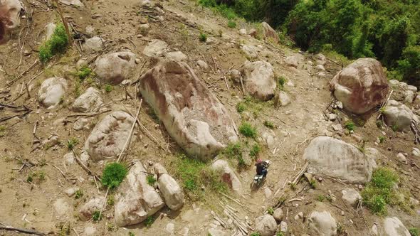 Aerial. Extreme Ride of a Dirt Biker on the Dangerous Hillside with Big Rocks. alt