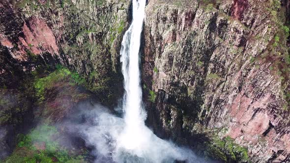 Drone flying towards huge waterfall, camera tilts down for amazing perspective. alt