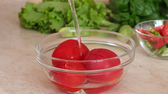 The cook blanchs tomatoes in a glass bowl with hot water. Pouring boiled hot water over a tomato.