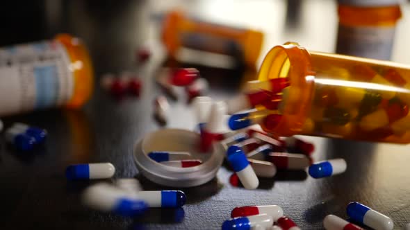 Prescription drugs with many pills and capsules spilling out of a medicine bottle in slow motion. alt