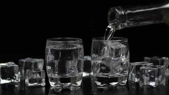 Pouring Up Two Shots of Vodka From a Bottle Into Glass. Black Background alt