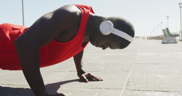 Focused african american man doing press ups, exercising outdoors by the seaside alt