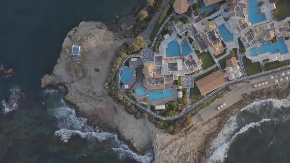Aerial view of resort hotel with swimming pool on rocky seashore foaming waves on beach Crete Greece