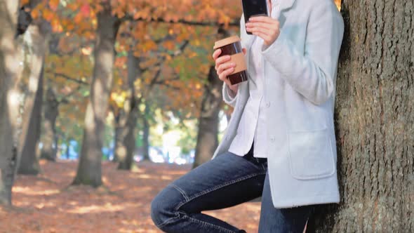 Young Beautiful Woman Drinks Coffee and Uses Smartphone