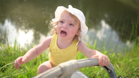 Little Funny Cute Blonde Girl Child Toddler in Yellow Bodysuit and White Hat Crying Trying Climb