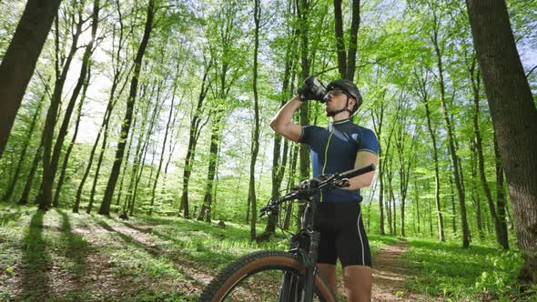 A Man on a Bicycle is Standing on a Forest Path alt