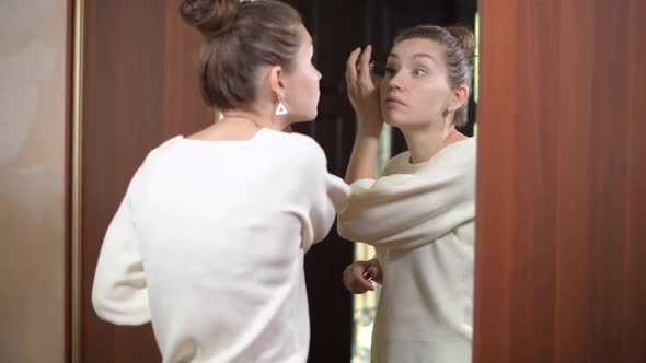 woman paints eyelashes in front of a mirror at home, going to a meeting alt