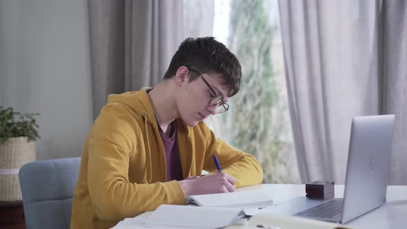 Camera Moving From Left To Right Around Young Caucasian Boy in Eyeglasses Writing and Using Laptop alt