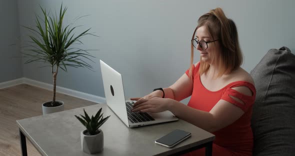 Caucasian Young Woman in the Red Dress Working By Laptop From Home Female Freelancer at Work Remote