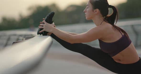 Sportswoman Warming Up Near Railing on Embankment alt