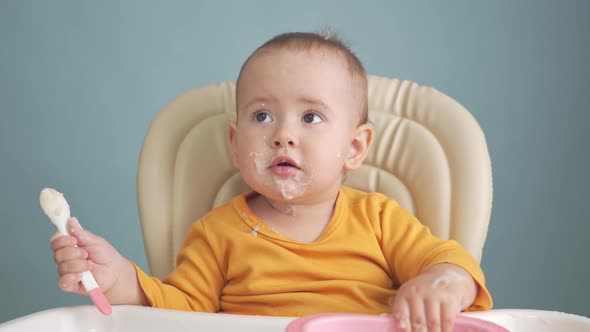 Toddler 12-18 months old eats oatmeal porridge moves the plate with his hands on the table. alt