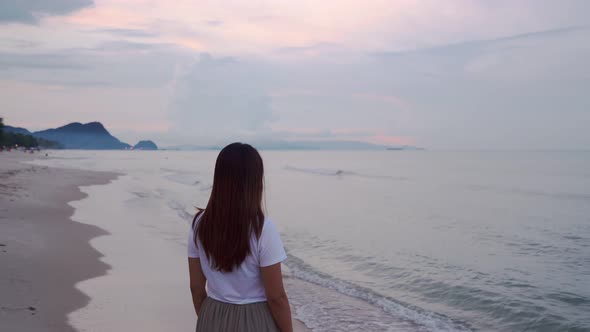 Lonely young asian woman walking on the beach at sunset