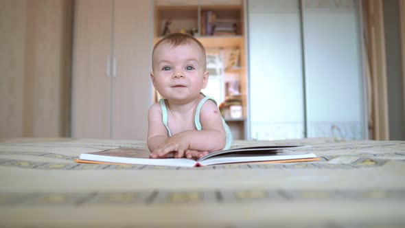 Cute Child Read a Book Lying on the Bed and Drool. Baby Turns the Pages. Development of a Little