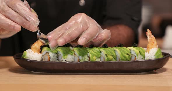 Chef Putting Roe (Black Sushi Caviar) In Slow Motion On Top Of Shrimp Tempura Sushi Rolls With Slice alt