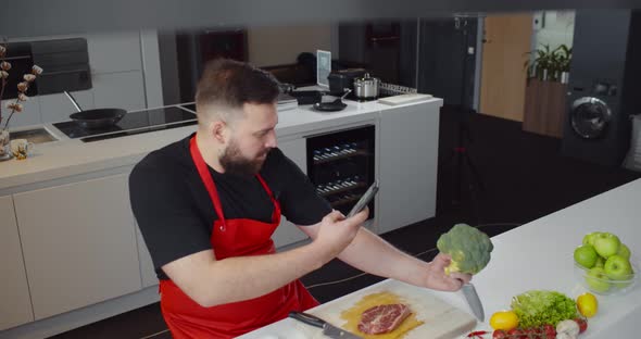 Young Man Cooking at Home and Taking Photo of Broccoli on Smartphone alt
