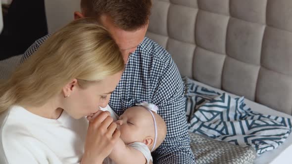Mother and Father Hugging and Admiring Their Baby While the Child Sleeps in the Arms of the Mother alt