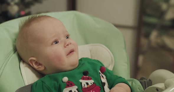 Capricious Christmas Toddler in Kid Chair During Feeding with Spoon By Mother alt