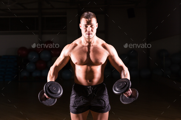 Muscular bodybuilder guy doing exercises with dumbbells.