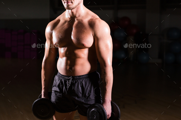 Muscular bodybuilder guy doing exercises with dumbbells.