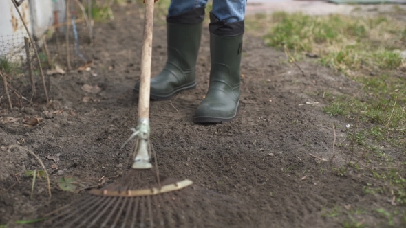Gardener Wearing Rubber Boots Raking Soil