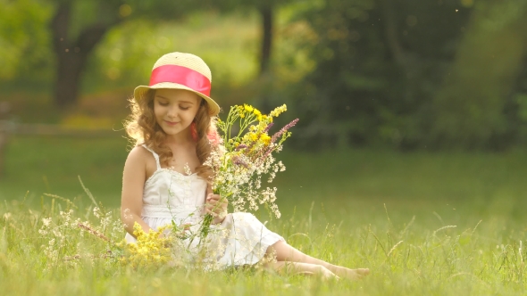 Child Holds a Bouquet of Wildflowers in Her Hands, She Smells Them and Smiles alt