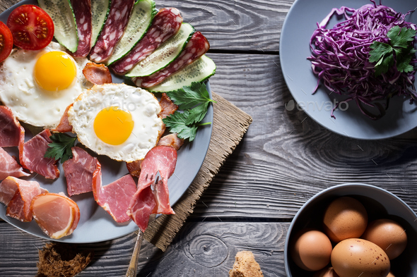 Fried eggs with vegetables and bacon on a wooden table - Stock Photo - Images