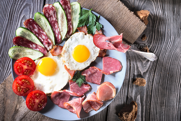 Fried eggs with bacon and vegetables on a wooden table - Stock Photo - Images
