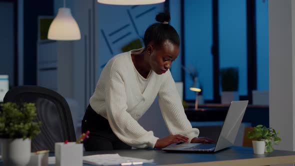 Manager Black Woman Standing at Desk Searching on Laptop and Looking at Camera alt
