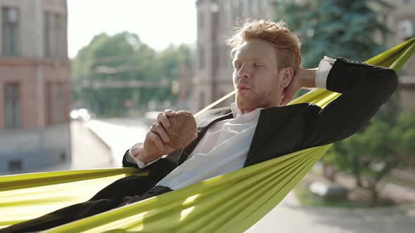 Successful Businessman Enjoying Coconut in Hammock Outdoors alt