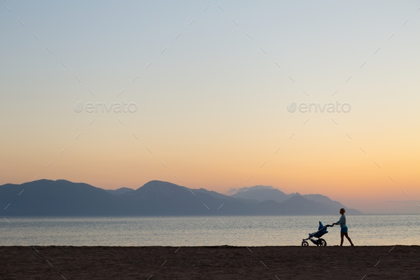 Silhouette of mother with stroller enjoying motherhood at sunset