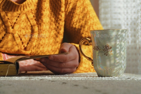 caucasian woman reading book and having tea at home