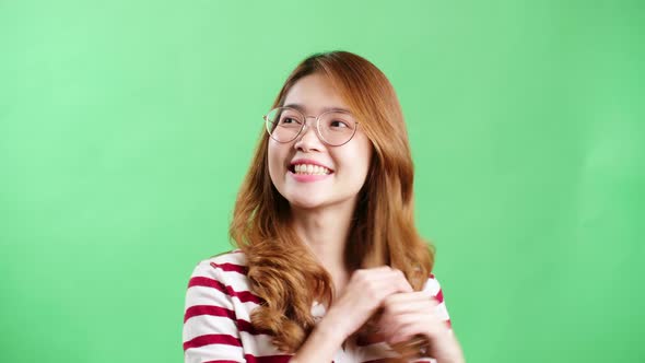 Happy playful Asian girl with eyeglasses smiling and playing with her hair over green screen. alt