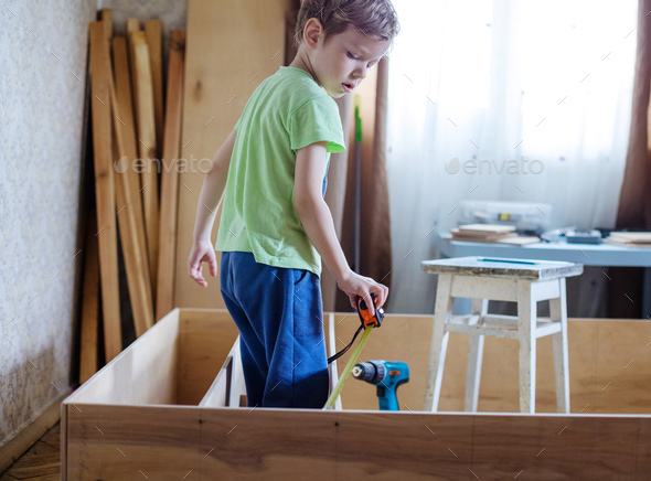 Young boy using reel to measure wooden bookcase or shelf unit