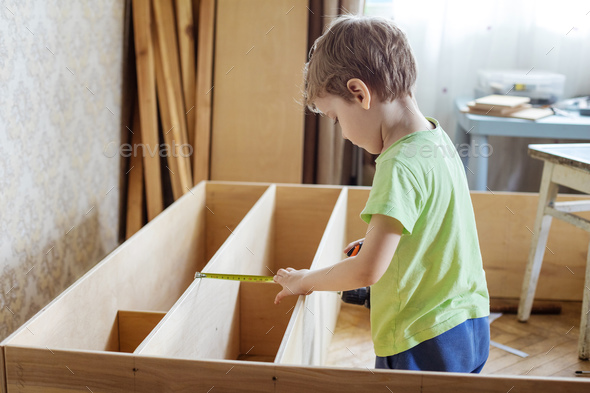 Young boy using reel to measure wooden shelf of bookcase