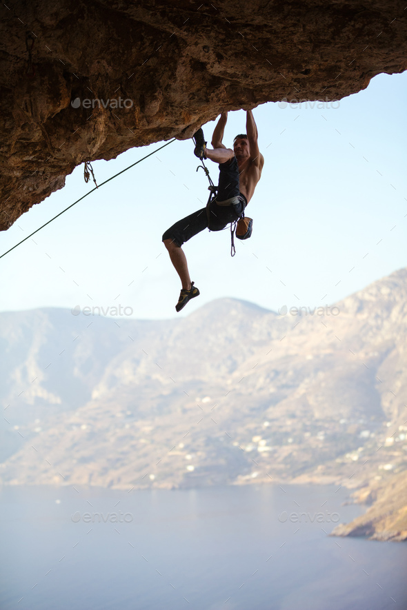 Young man struggling to climb ledge on cliff