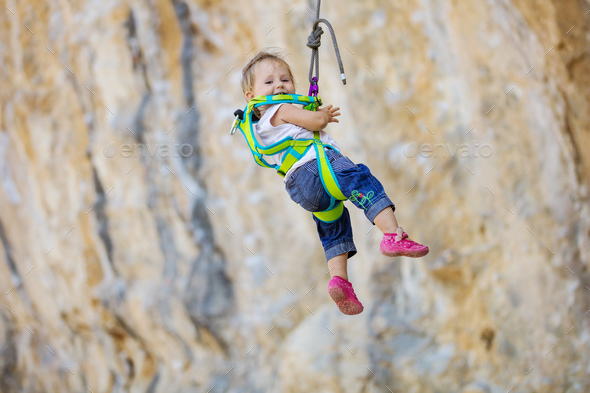 Little girl in climbing gear hanging on rope