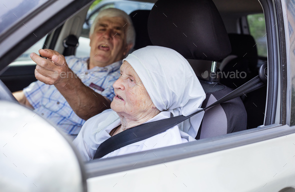Senior woman taking driving lesson, male instructor pointing angrily at something