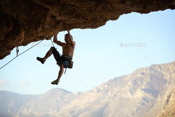 Young man struggling to climb ledge on natural cliff