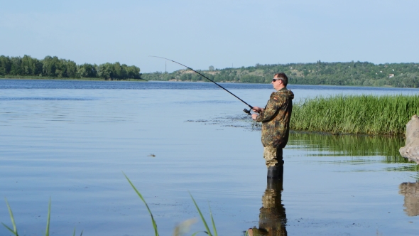 Fisherman Stands Knee Deep in the River, He Has a Fish Bite alt