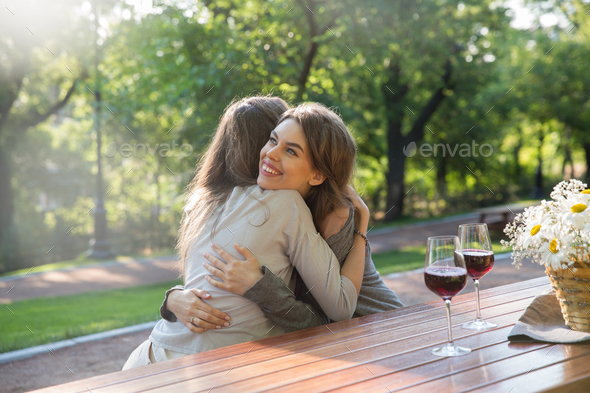 Happy young two women sitting outdoors in park drinking wine