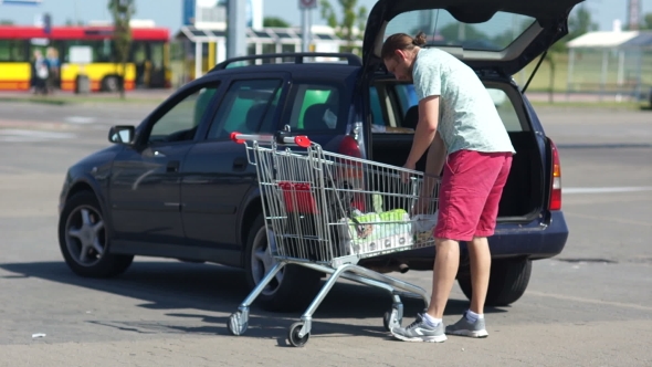 A Men Loading Foods From Shopping Cart Into Car Trunk at Parking Lot alt