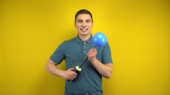 A Young Man Inflates a Blue Balloon with a Pump on a Yellow Background. Man in a Green Polo.