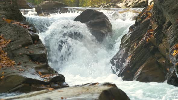 A Small Mountain Stream with Fast Moving Clear Water Between Rocky Stones in Autumn alt