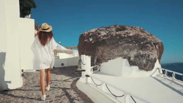 Young Sexy Woman Is on the Greek Island Santorini in a White Dress and and Straw Hat White Greek