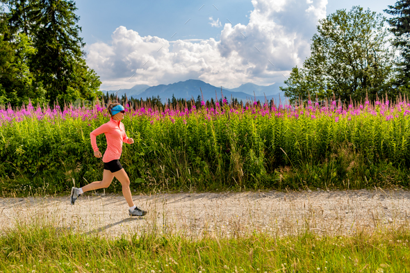 Woman trail running on country road in mountains, summer day